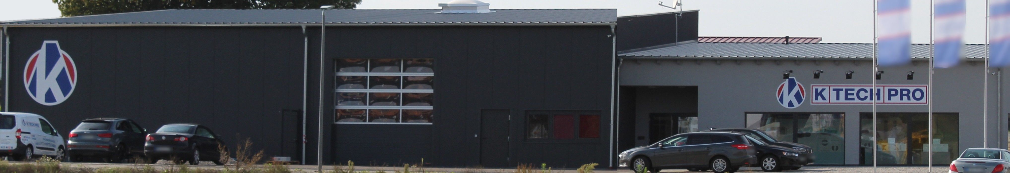 Südostseite des Firmengebäudes in Wilting im September 2018: dunkle Halle mit Rolltor, rechts das helle Bürogebäude mit Firmenschild
