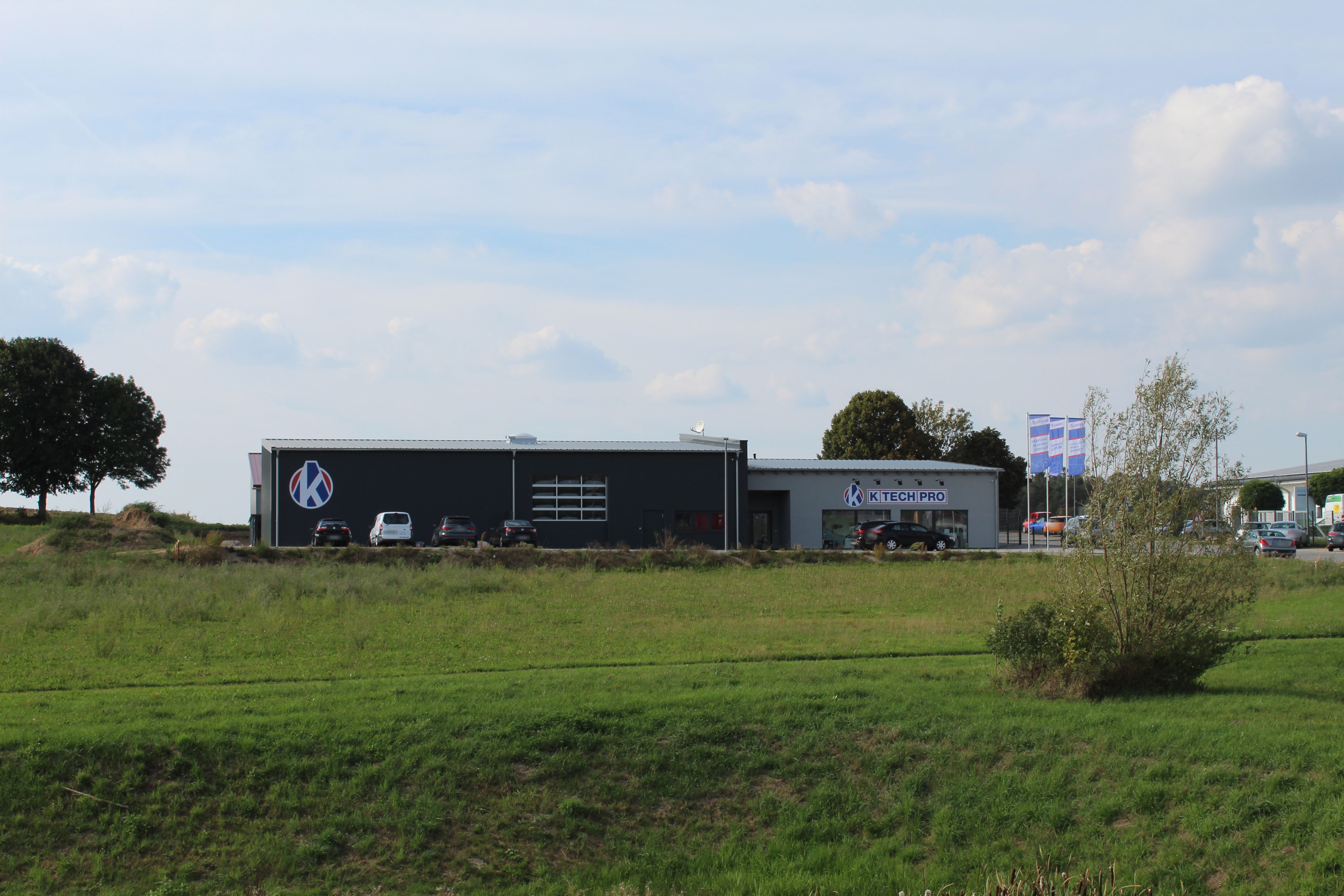 Das Firmengebäude der K-TECH-PRO GmbH in Wilting, von einer Wiese aus gesehen, darüber weiter Himmel